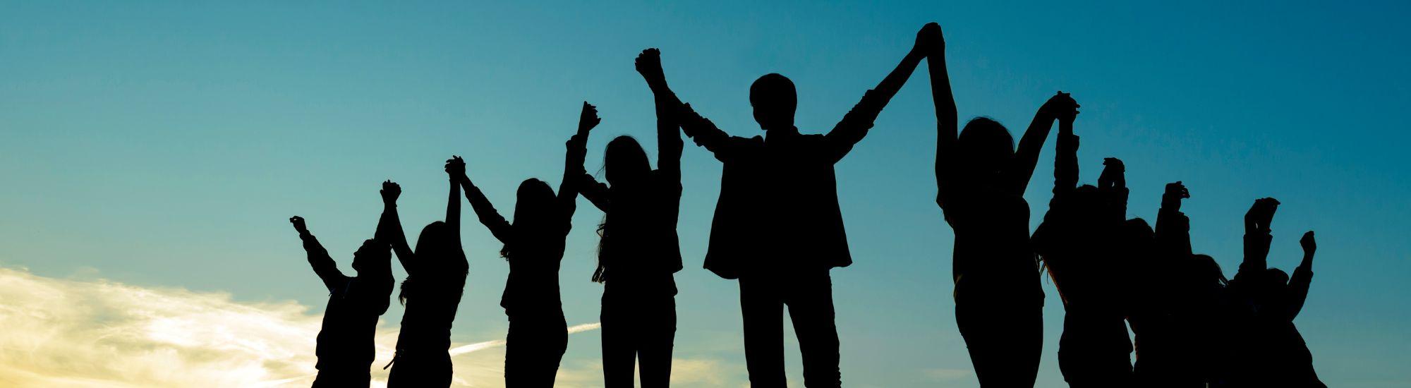 ten shadowed people standing with arms raised holding hands against a blue sky